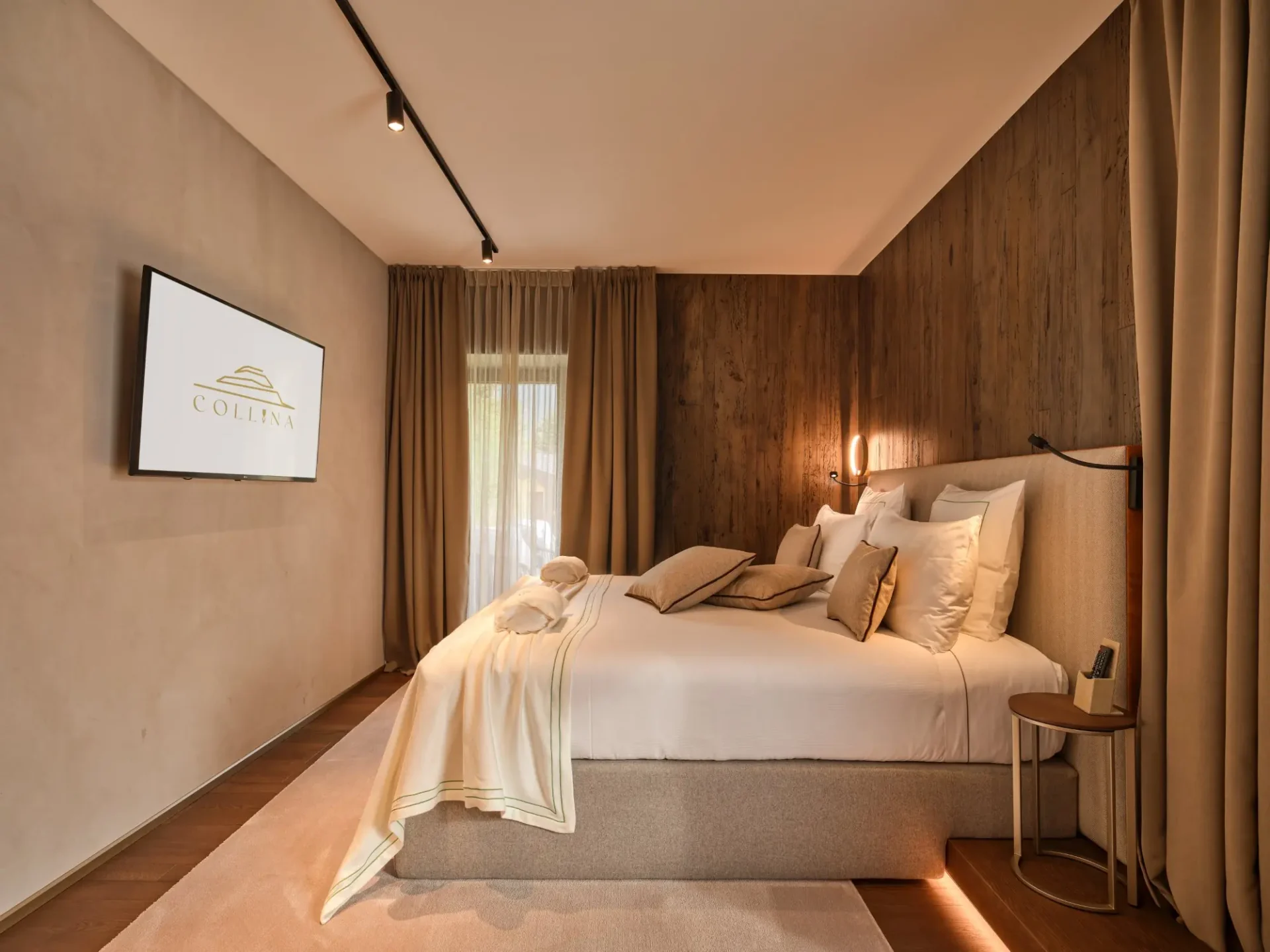 Junior Suite con letto king size, parete in legno di cirmolo e logo Collina su TV. Collina Luxury Relais, Clusone