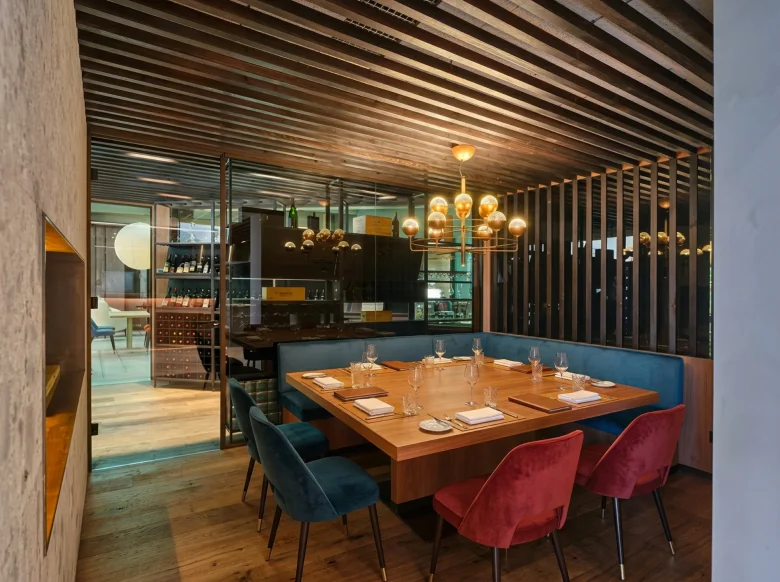 Tavolo privato con poltrone in velluto blu e rosso, lampadario dorato e cantina vini a vista al Beides Restaurant del Collina Luxury Relais di Clusone