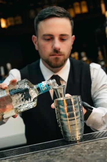 Barman in gilet nero che versa spirits nello shaker al bancone dell'Americano Bar del Collina Luxury Relais di Clusone