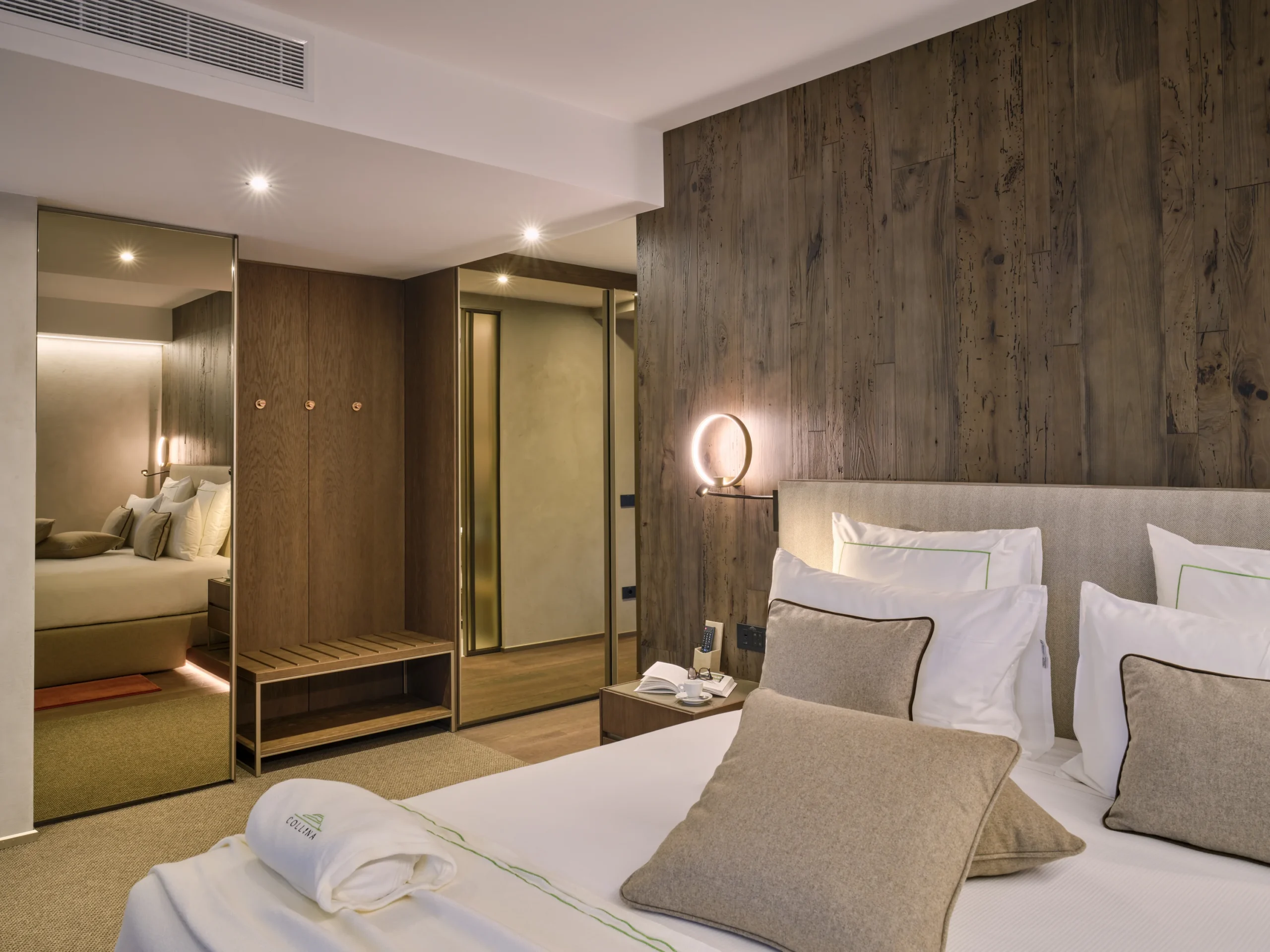 Camera con letto king-size, cuscini beige e rosso, armadio a specchio bronzo e parete in legno antico
