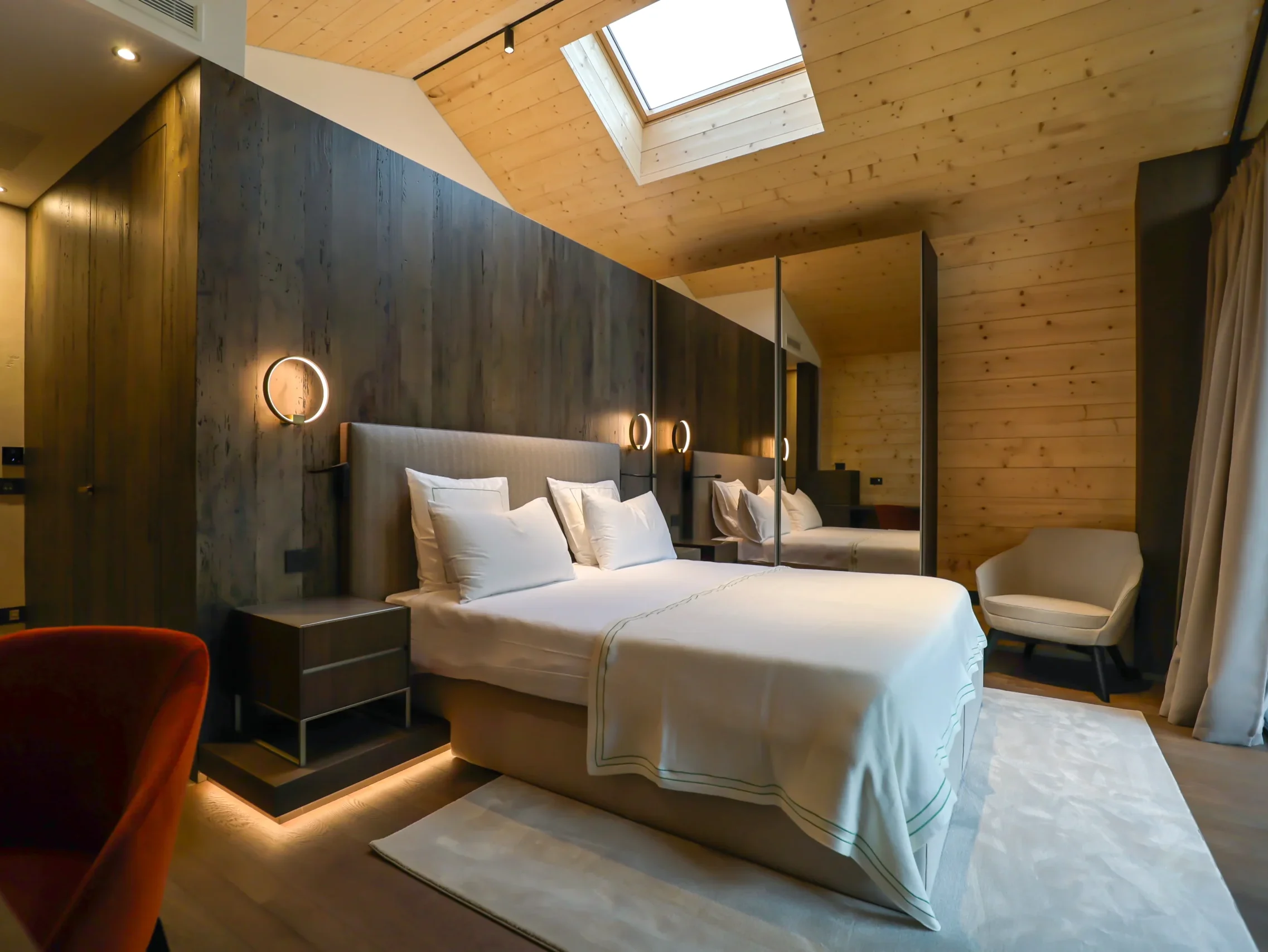 Camera chalet con letto king-size, testata in legno scuro, lucernario sul soffitto in legno chiaro e specchio a muro