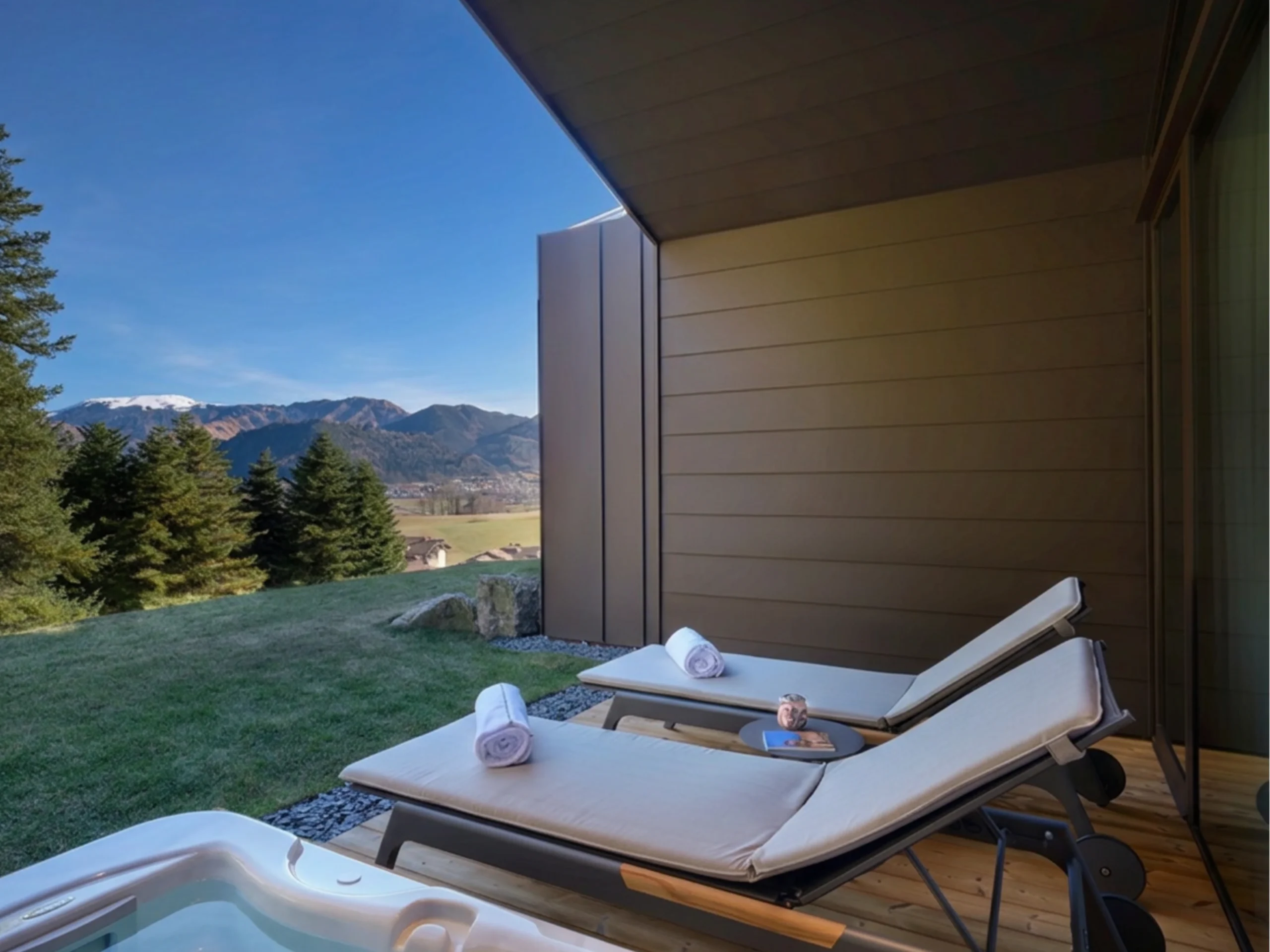 Veranda chalet in legno con jacuzzi privata, due lettini con asciugamani e vista panoramica sulle Orobie