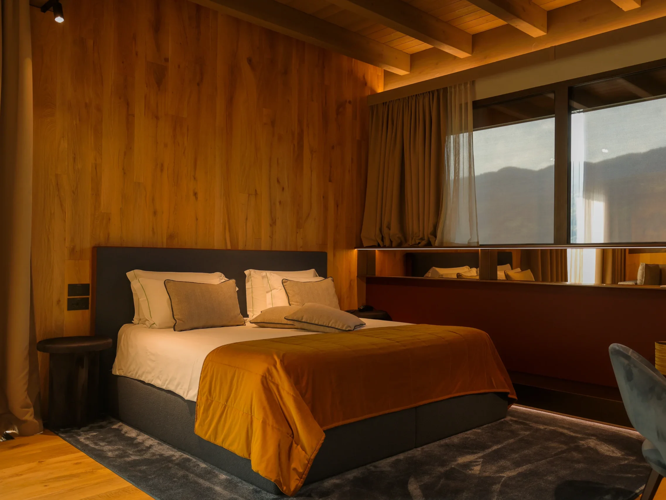 Camera da letto Penthouse con letto king-size, coperta senape, parete in rovere chiaro e finestra panoramica sulle montagne