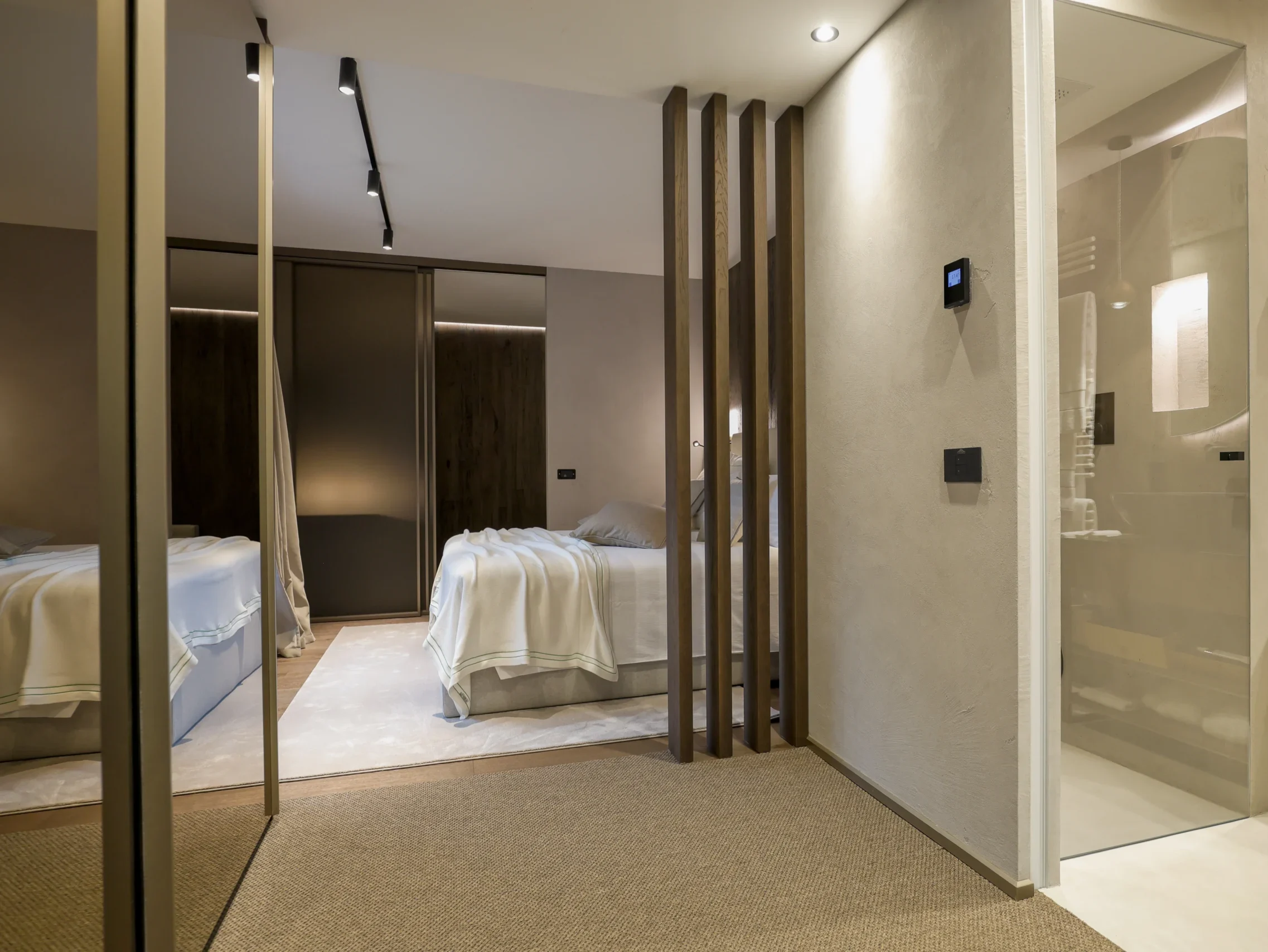 Vista dell'ingresso della Junior Suite con divisori in legno, camera da letto e bagno con doccia walk-in visibili