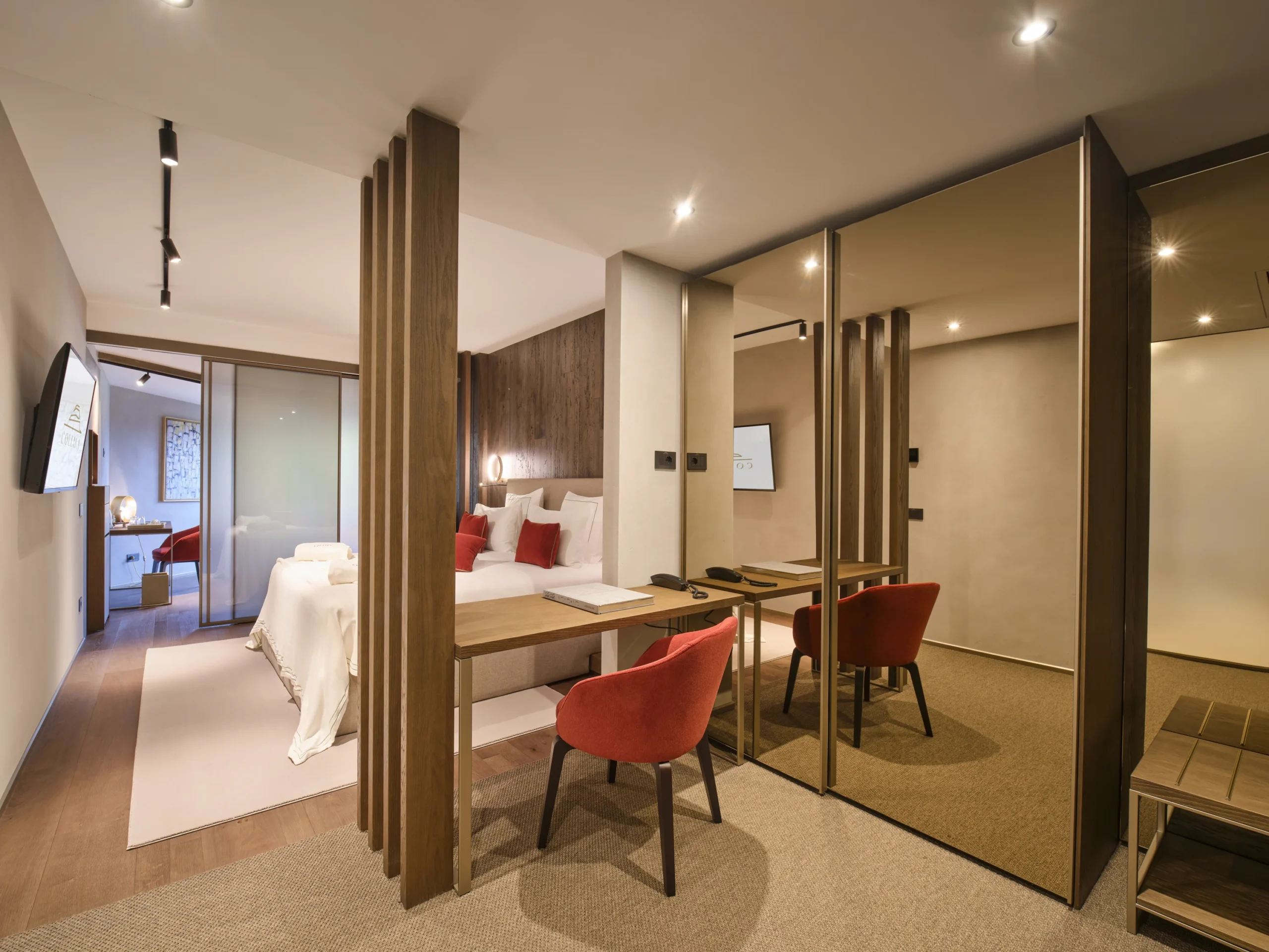 Signature Suite con letto, cuscini rossi, scrivania in legno con sedia rossa e parete a specchio bronzo