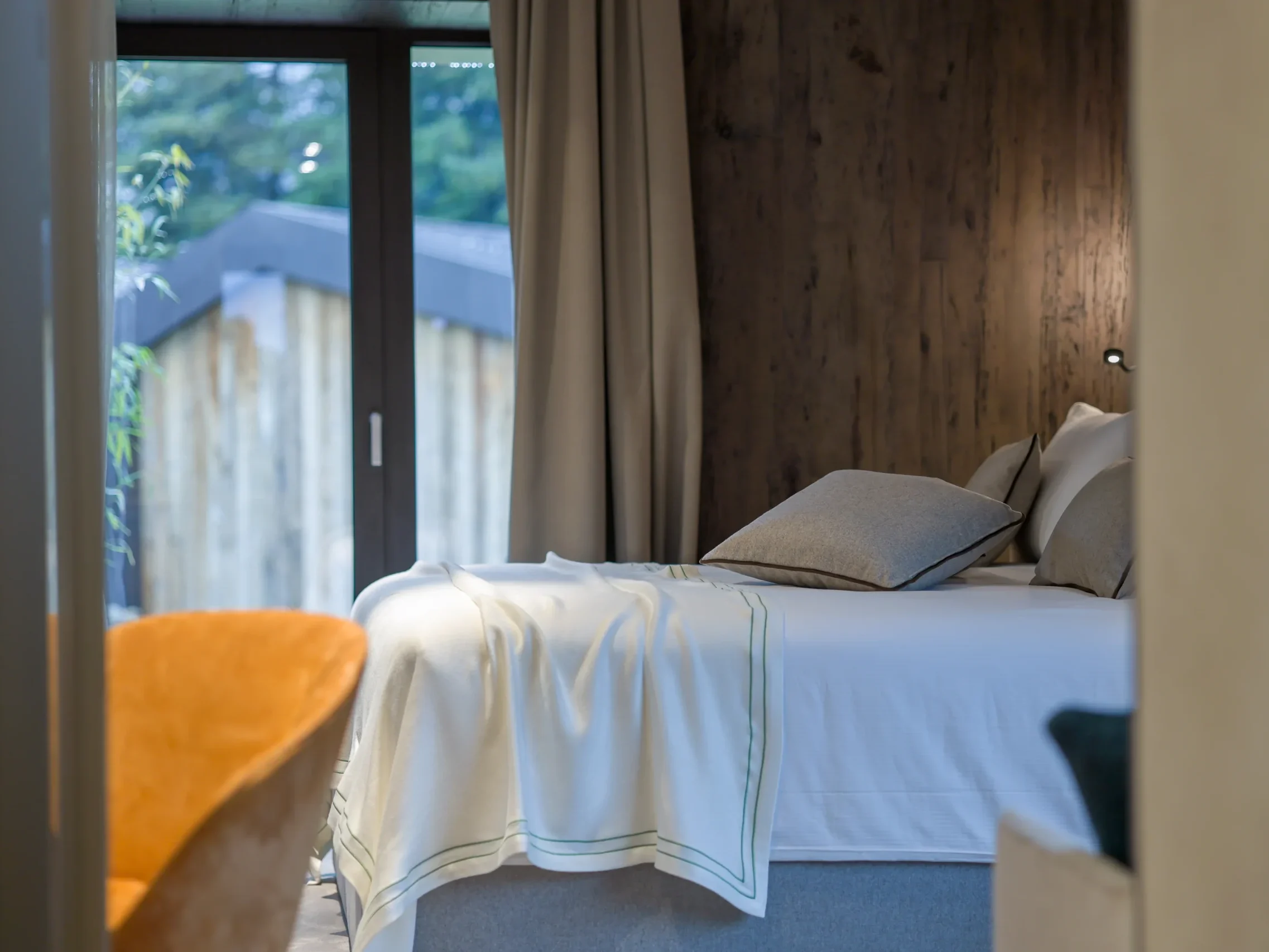 Dettaglio letto Junior Suite con cuscini grigi, coperta bianca e vetrata sul giardino con bambù