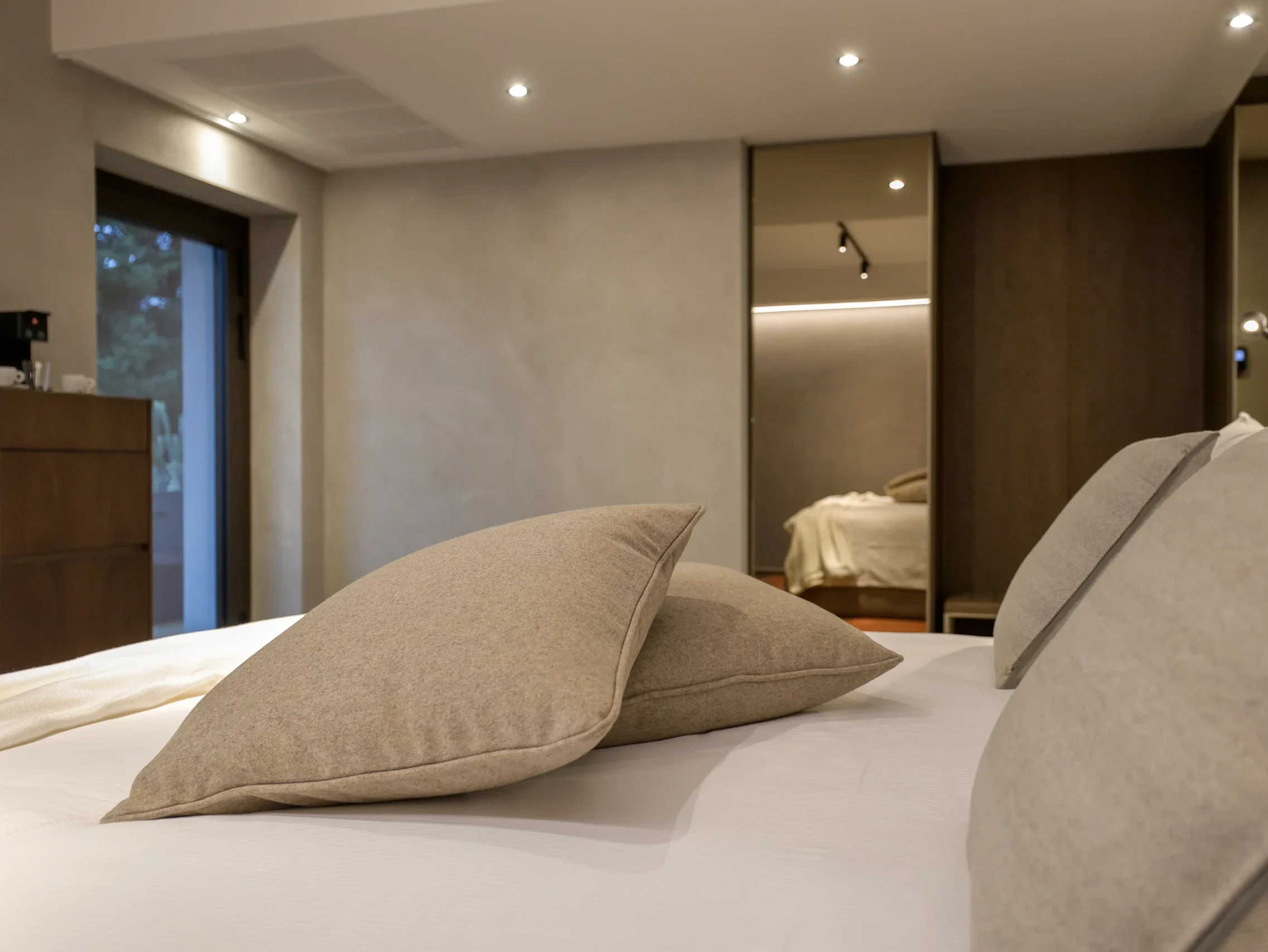 Camera Junior Suite con letto king-size, cuscini beige, armadio a specchio bronzo e riflesso della stanza