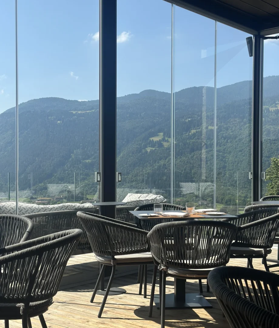 Terrazza con poltrone in corda, tavoli apparecchiati, pavimento in legno e vetrate panoramiche sulla Valseriana al Collina Luxury Relais di Clusone